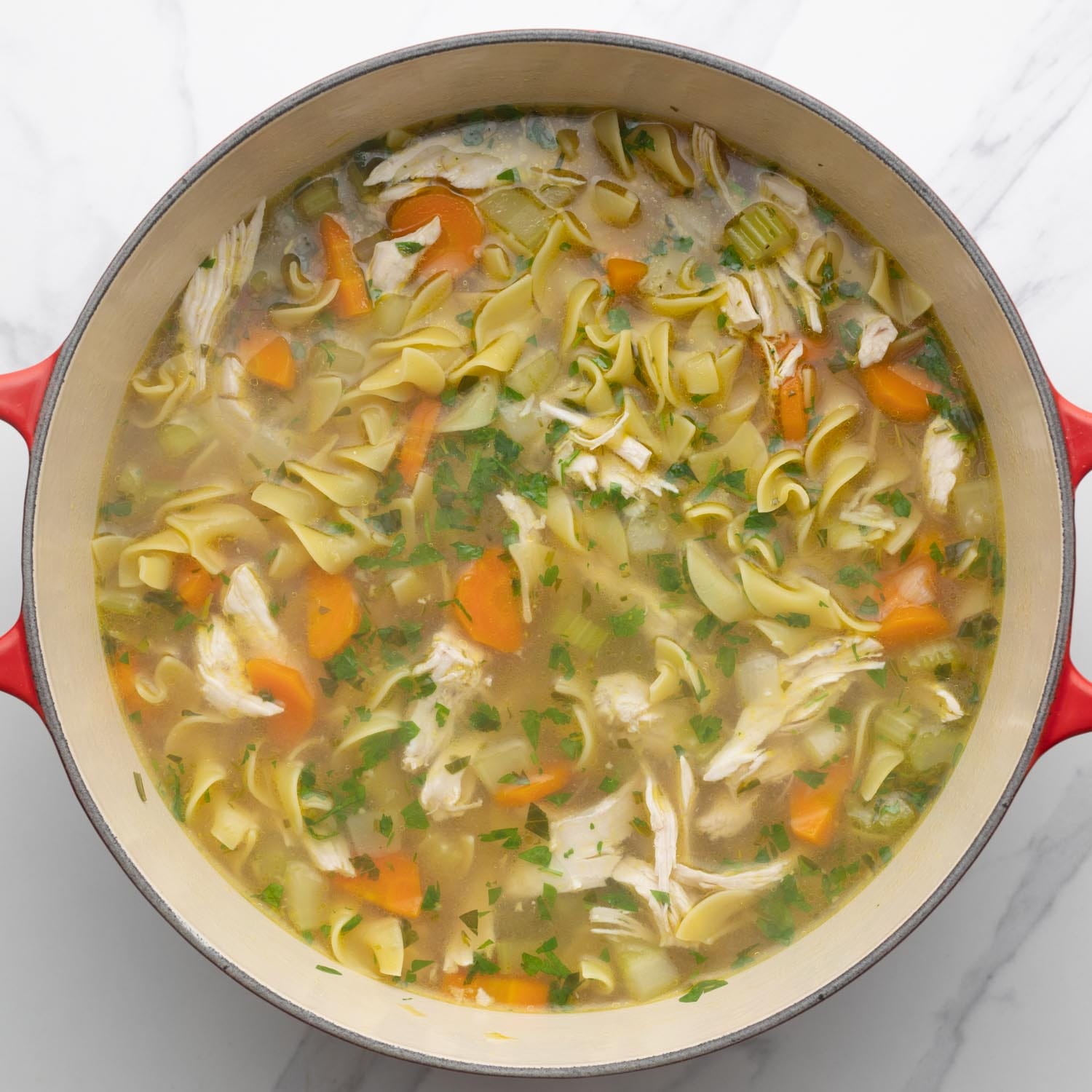 Chicken soup cooking in a dutch oven with red handles.