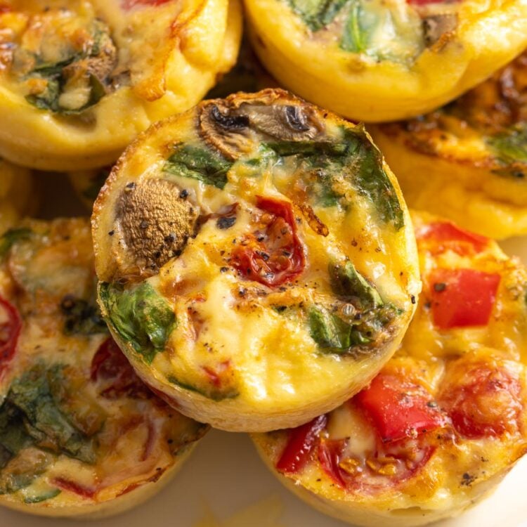 a plate stacked with egg muffins with tomatoes, peppers, mushrooms, and spinach.