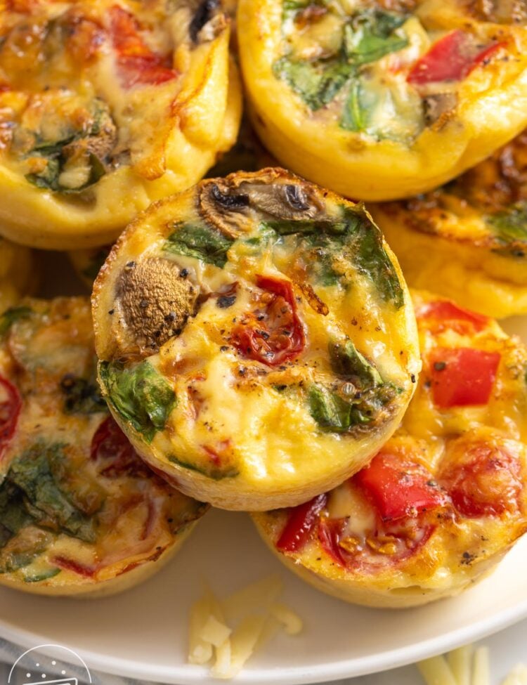 a plate stacked with egg muffins with tomatoes, peppers, mushrooms, and spinach.