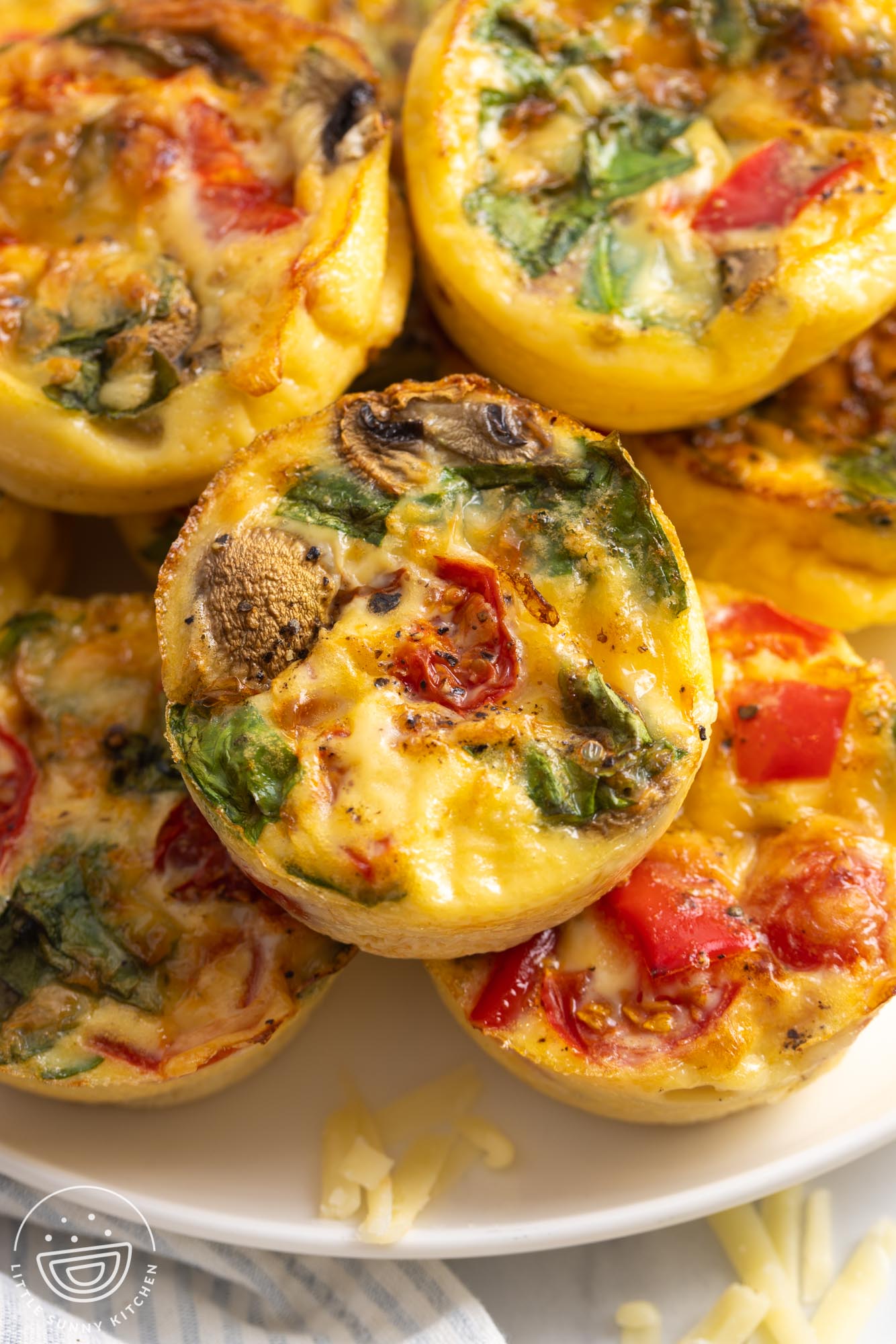 a plate stacked with egg muffins with tomatoes, peppers, mushrooms, and spinach.