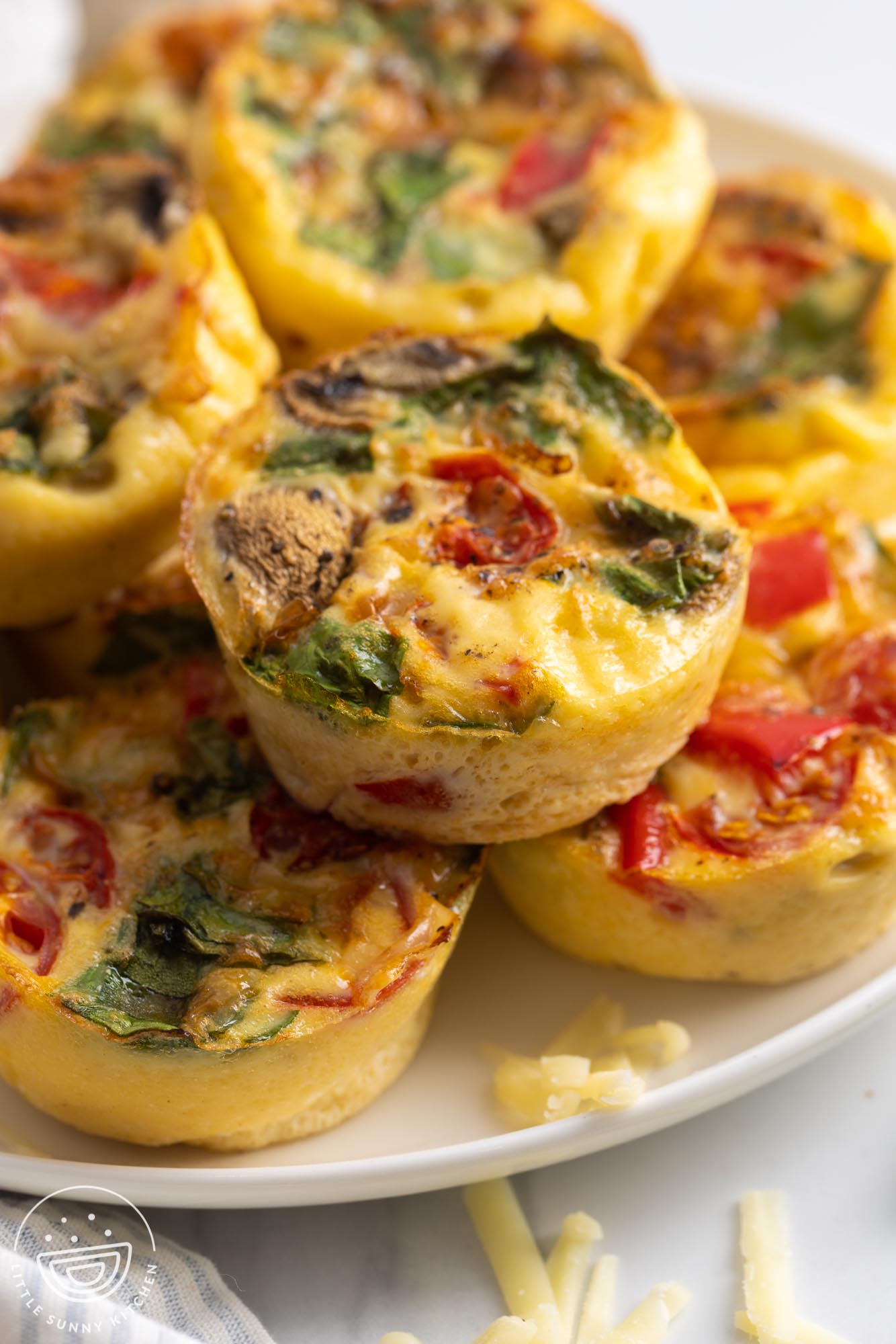 a plate stacked with several egg muffins with tomatoes, peppers, mushrooms, and spinach.