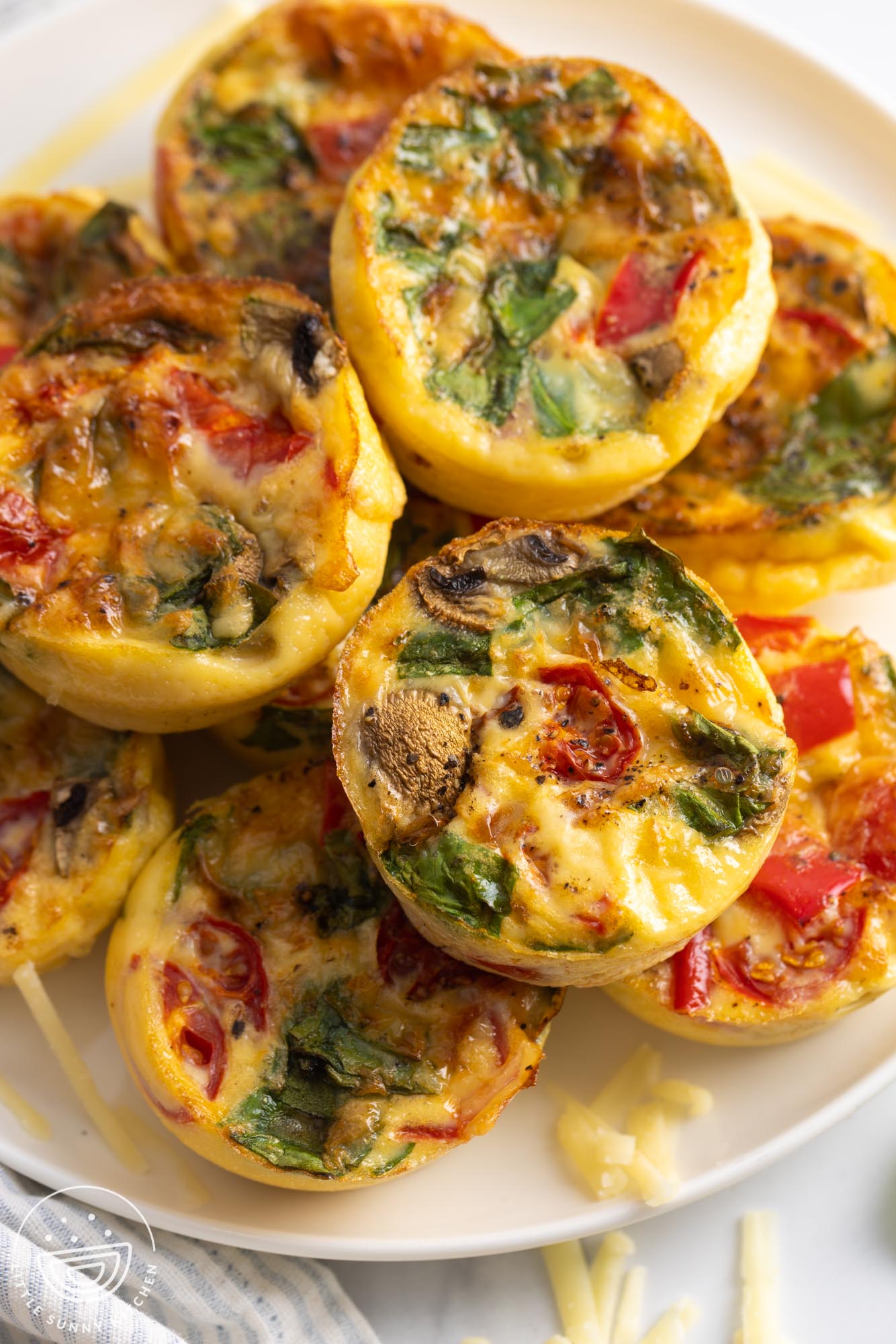 overhead view of a plate of baked egg muffins with vegetables and cheese inside.