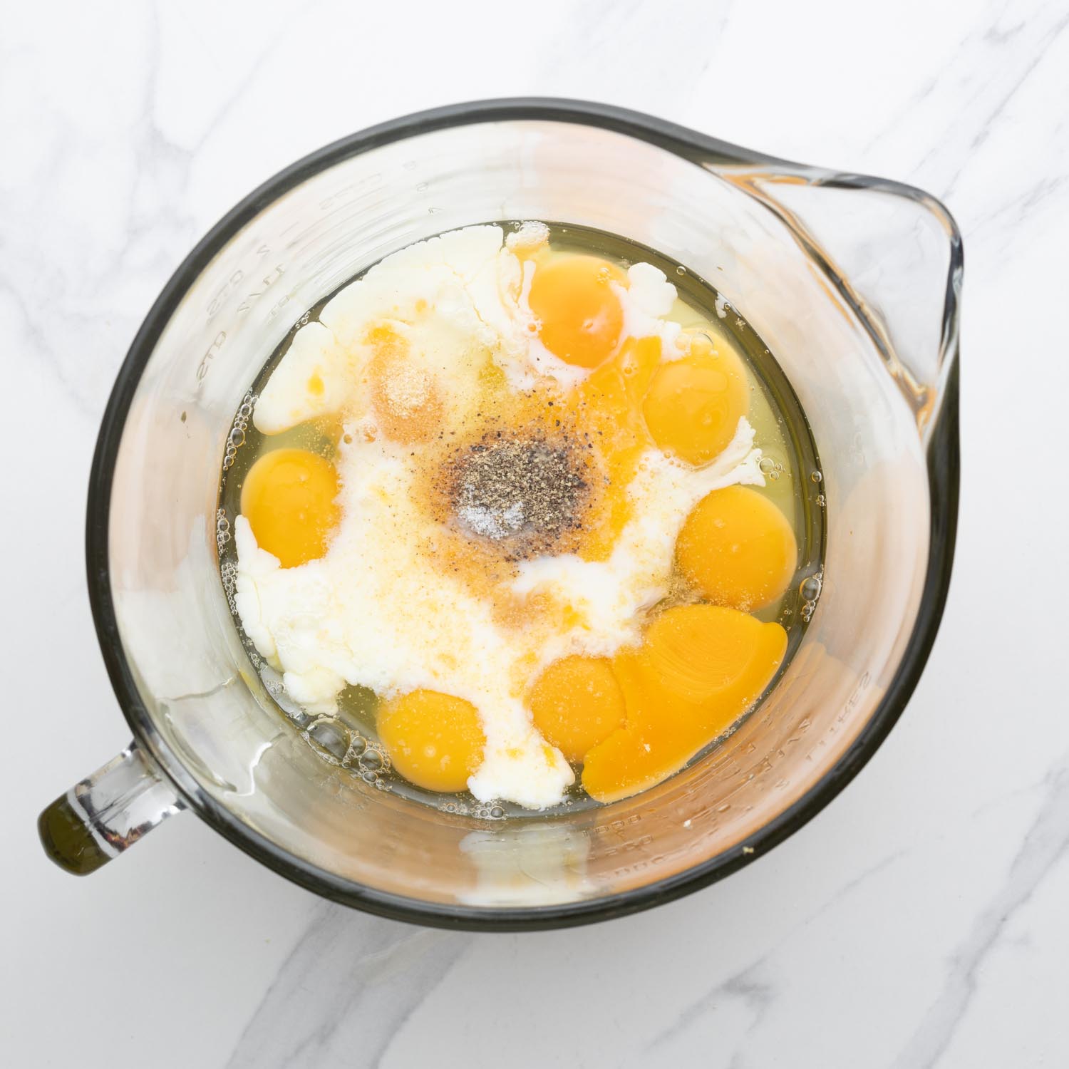 eggs, milk, salt, and pepper in a large glass measuring jug, viewed from overhead.