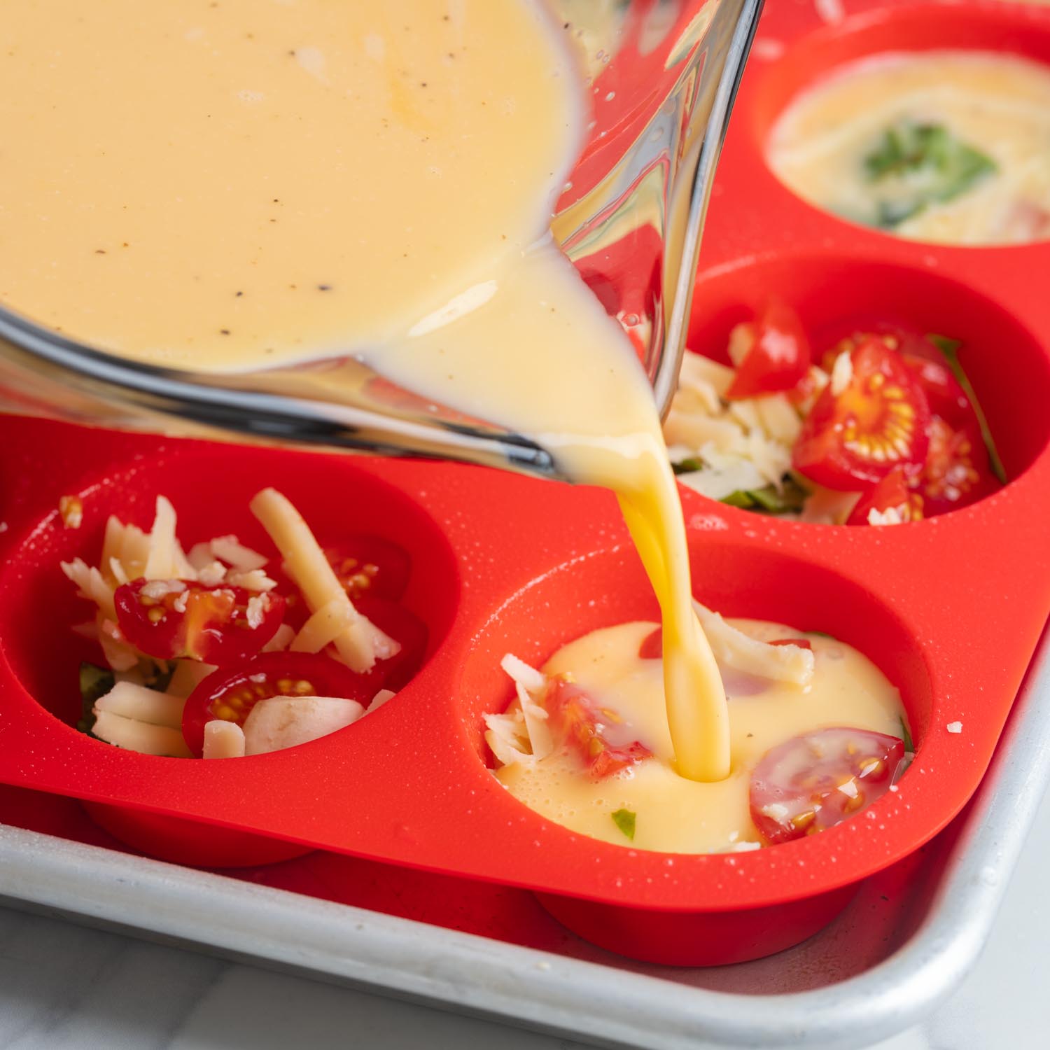 egg mixture poured carefully into a silicone muffin pan filled with cheese and veggies.