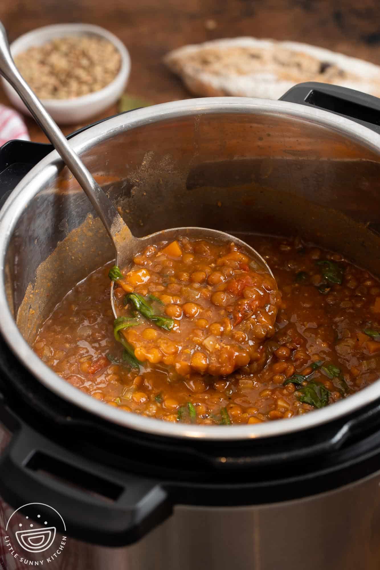 Lentil soup with spinach in an instant pot, served with a ladle.