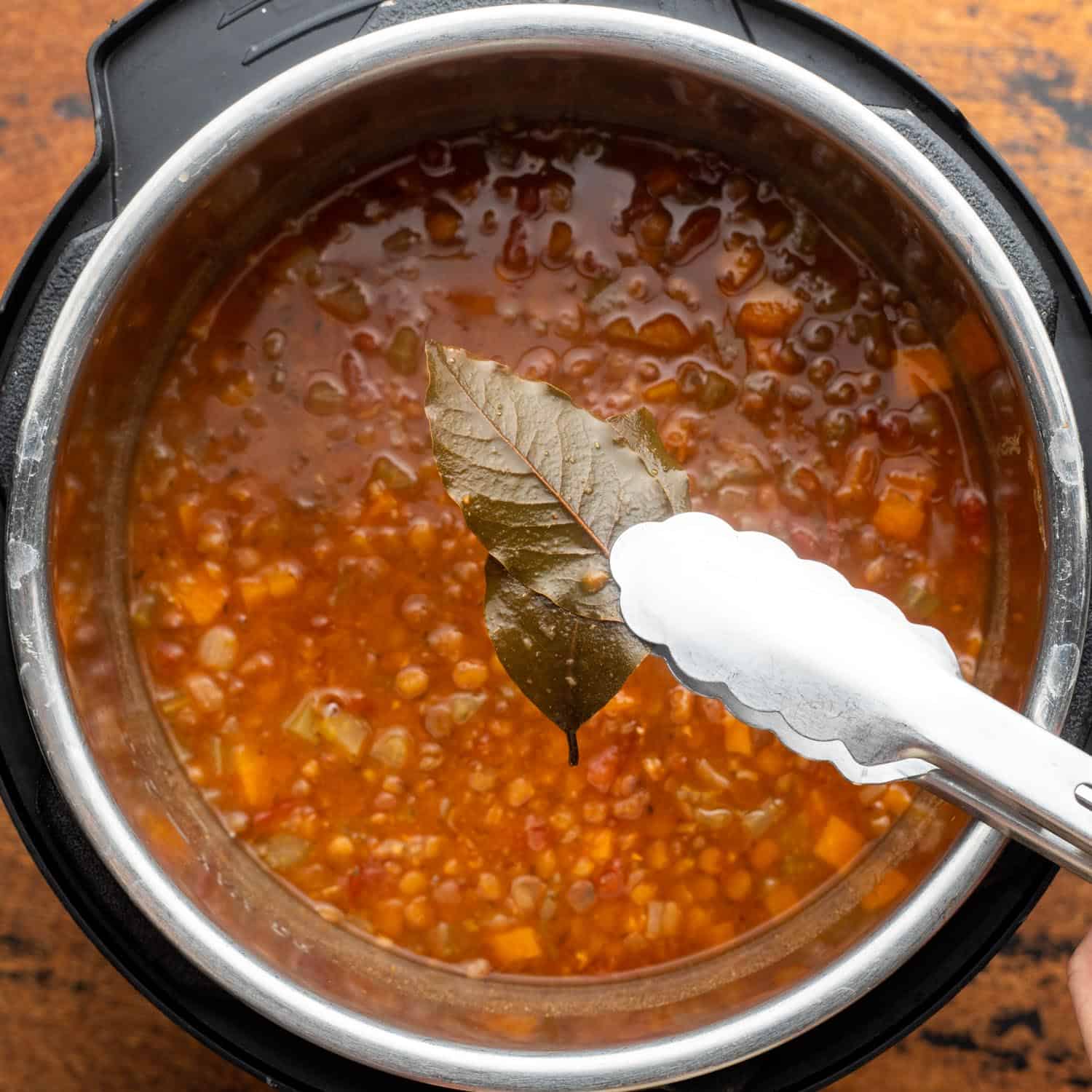 tongs removing two bay leaves from an instant pot of homemade lentil soup.