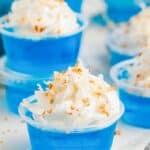 blue jack frost jello shots in plastic cups with whipped cream and coconut.