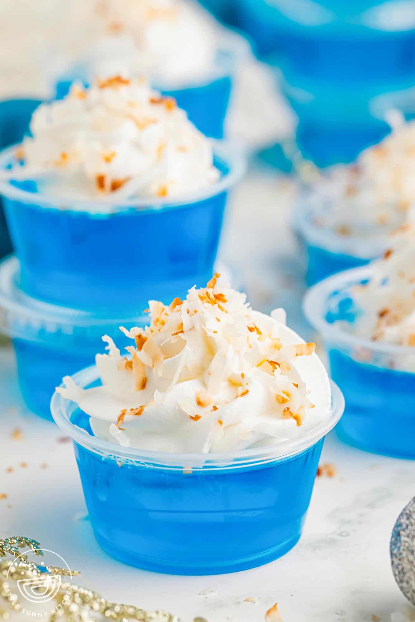 blue jack frost jello shots in plastic cups with whipped cream and coconut.