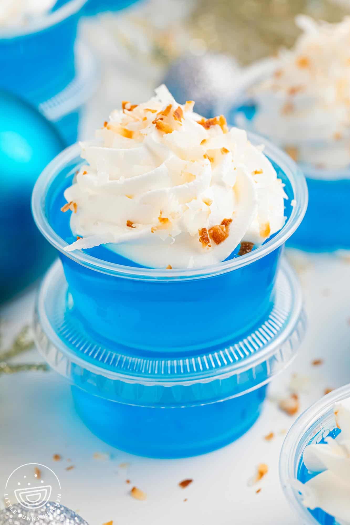 Blue jello shots for christmas topped with whipped cream and toasted coconut.