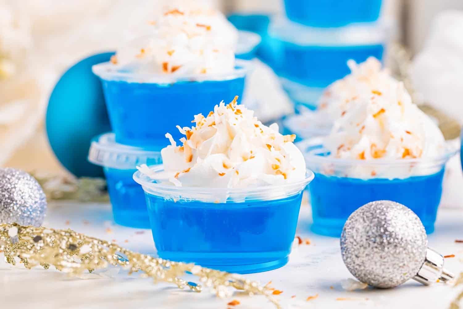 closeup of blue pineapple jello shots topped with whipped cream and toasted coconut.