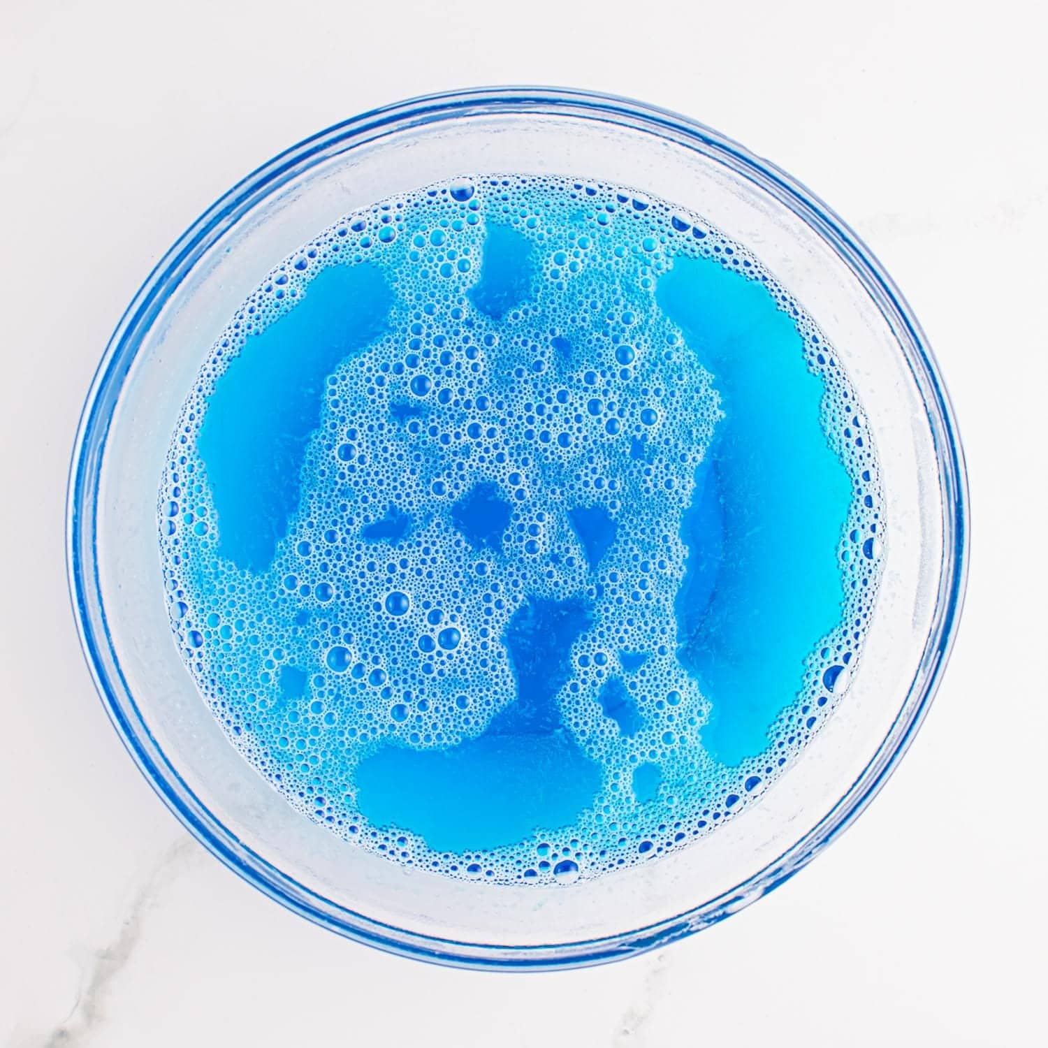 blue jello mixed with boiling water in a glass bowl.