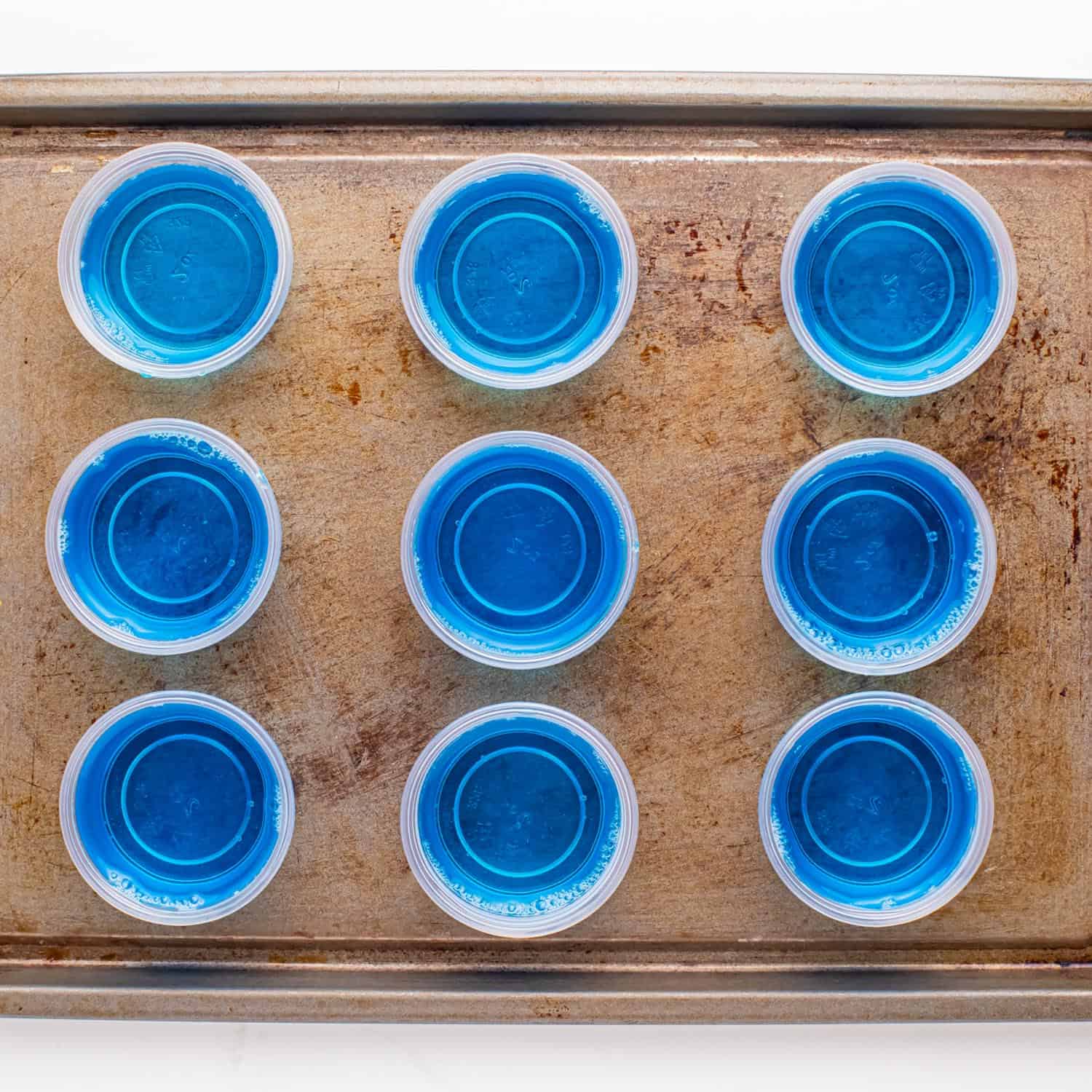 blue jello shots poured into 2 ounce disposable plastic cups on a sheet pan.