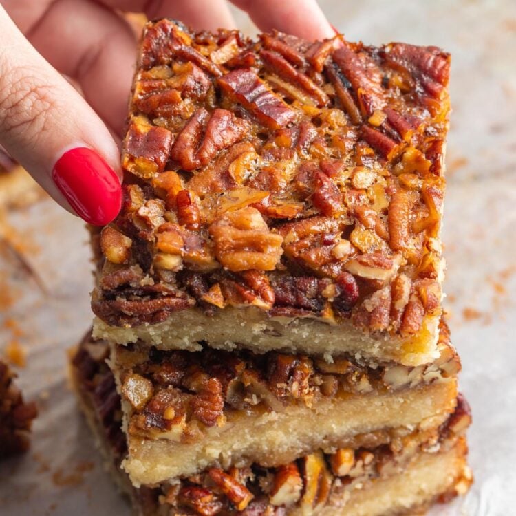 Three shortbread pecan bars stacked. A hand is picking one off the top of the pile.