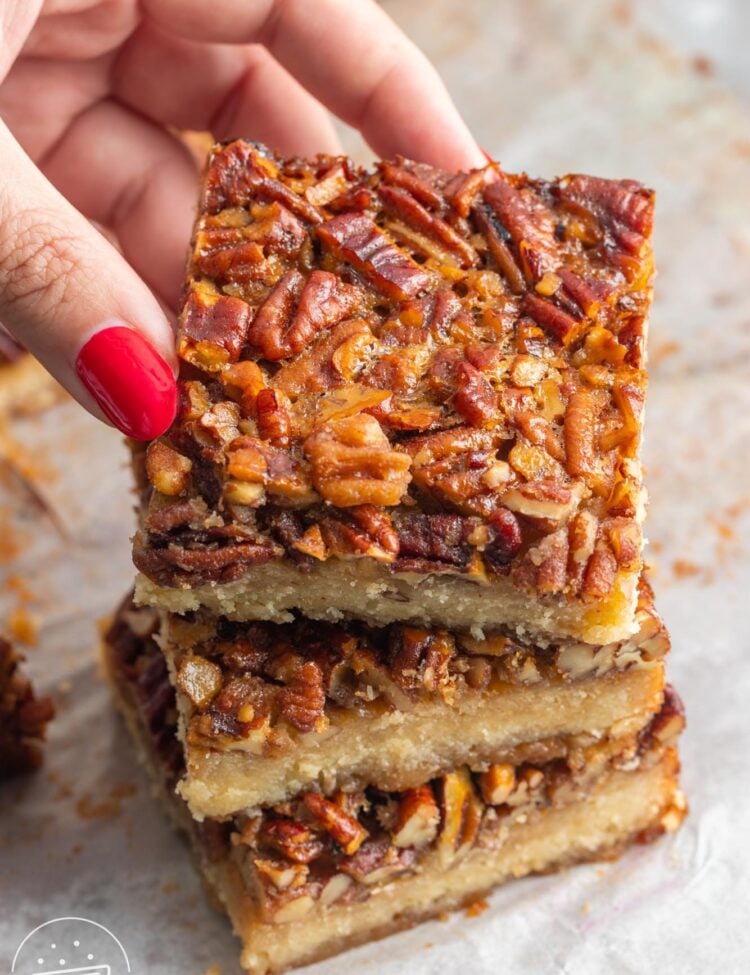 Three shortbread pecan bars stacked. A hand is picking one off the top of the pile.