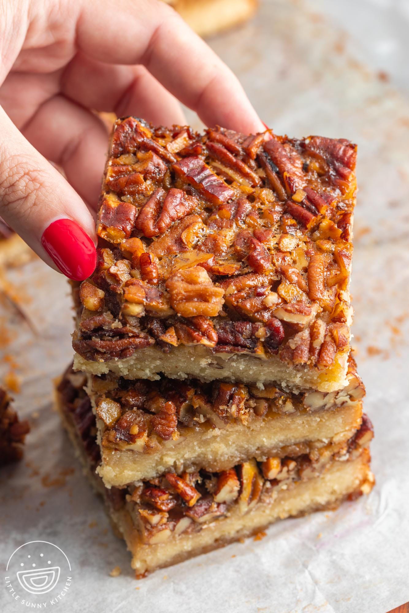 Three shortbread pecan bars stacked. A hand is picking one off the top of the pile.