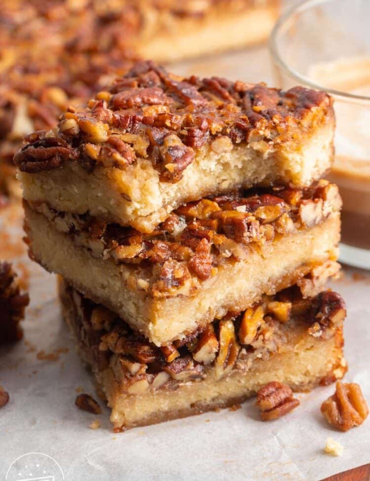 Three pecan pie bars in a stack. The top one has a bite taken to show the tender shortbread layer underneath the pecans.