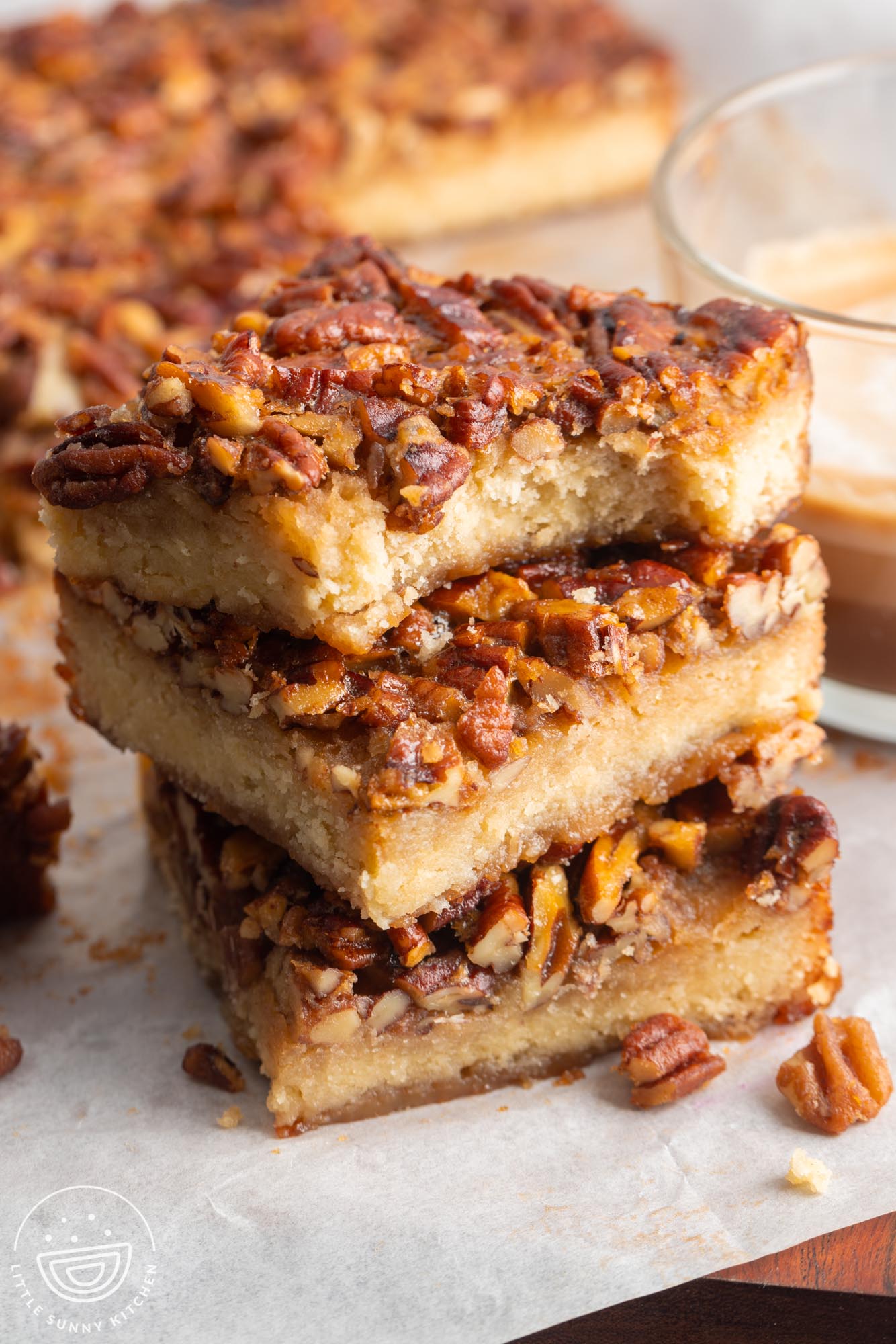 Three pecan pie bars in a stack. The top one has a bite taken to show the tender shortbread layer underneath the pecans.