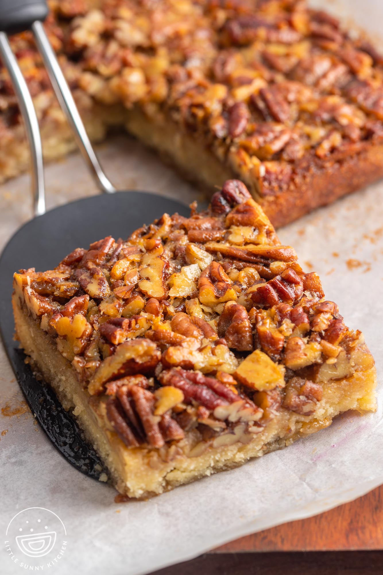 a black spatula lifting up a pecan pie bar from a piece of parchment paper.