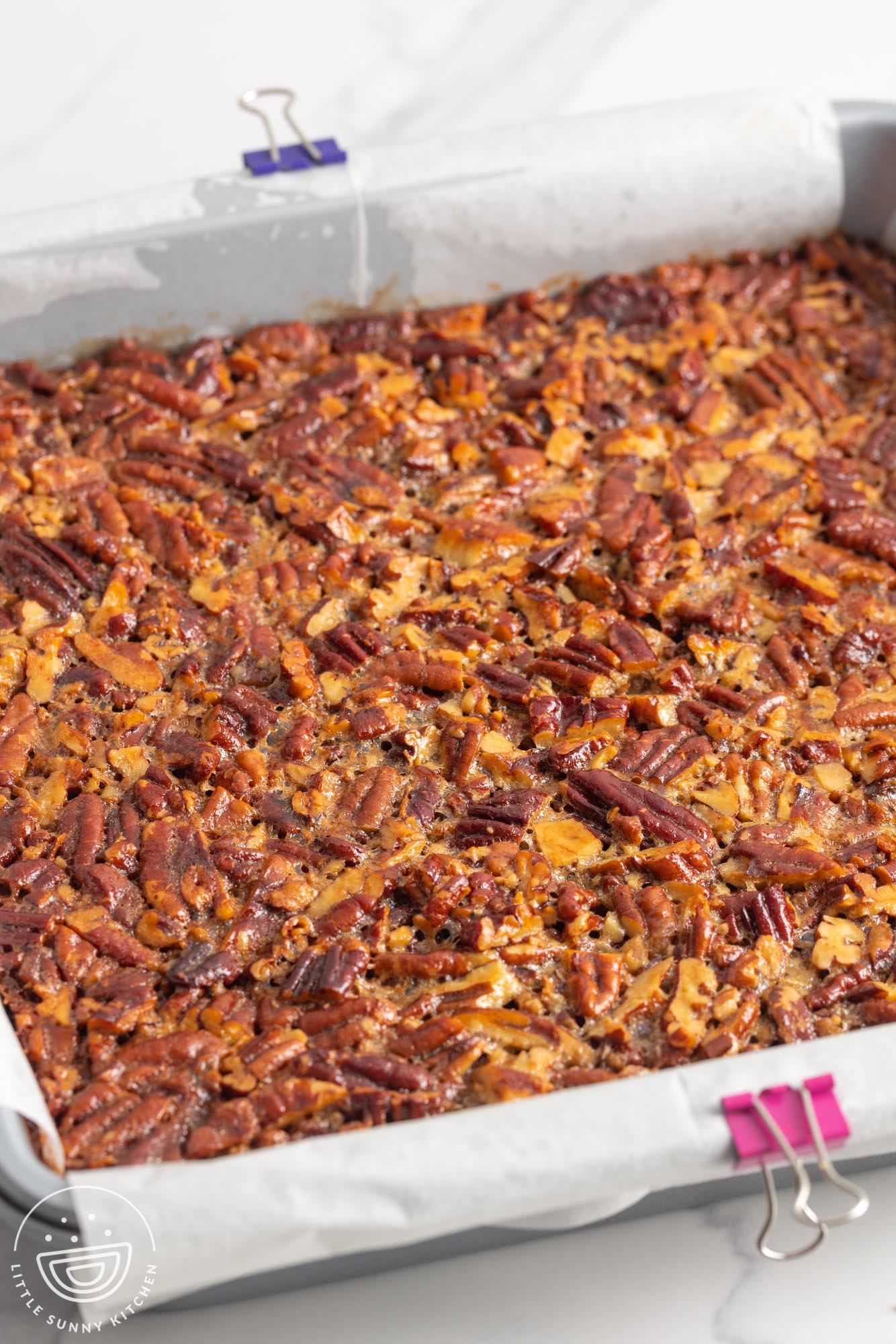 baked pecan pie bars in a metal pan lined with parchment paper.