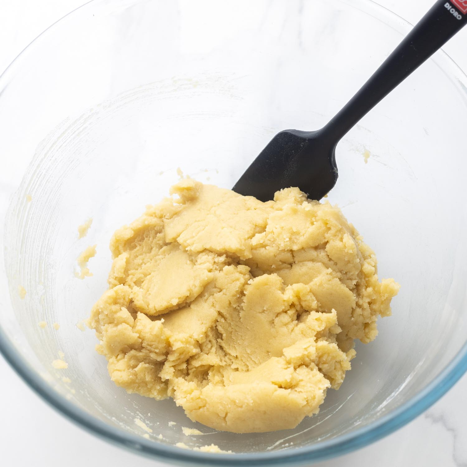 crust mixture for pecan pie bars in a glass mixing bowl with a black spatula.