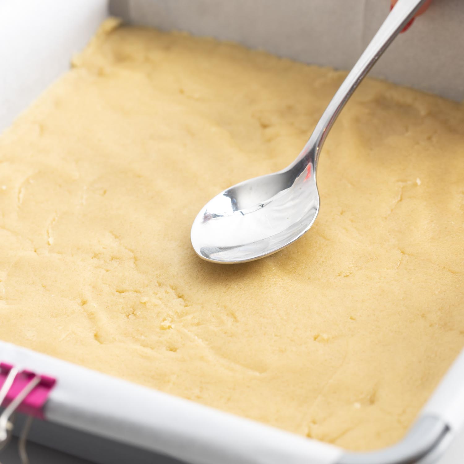 a teaspoon pressing down the dough mixture into a pan to create the base layer for pecan pie bars.