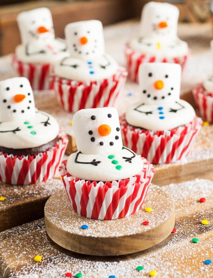 chocolate Snowman cupcakes made with marshmallow faces sitting on a wooden cutting board.