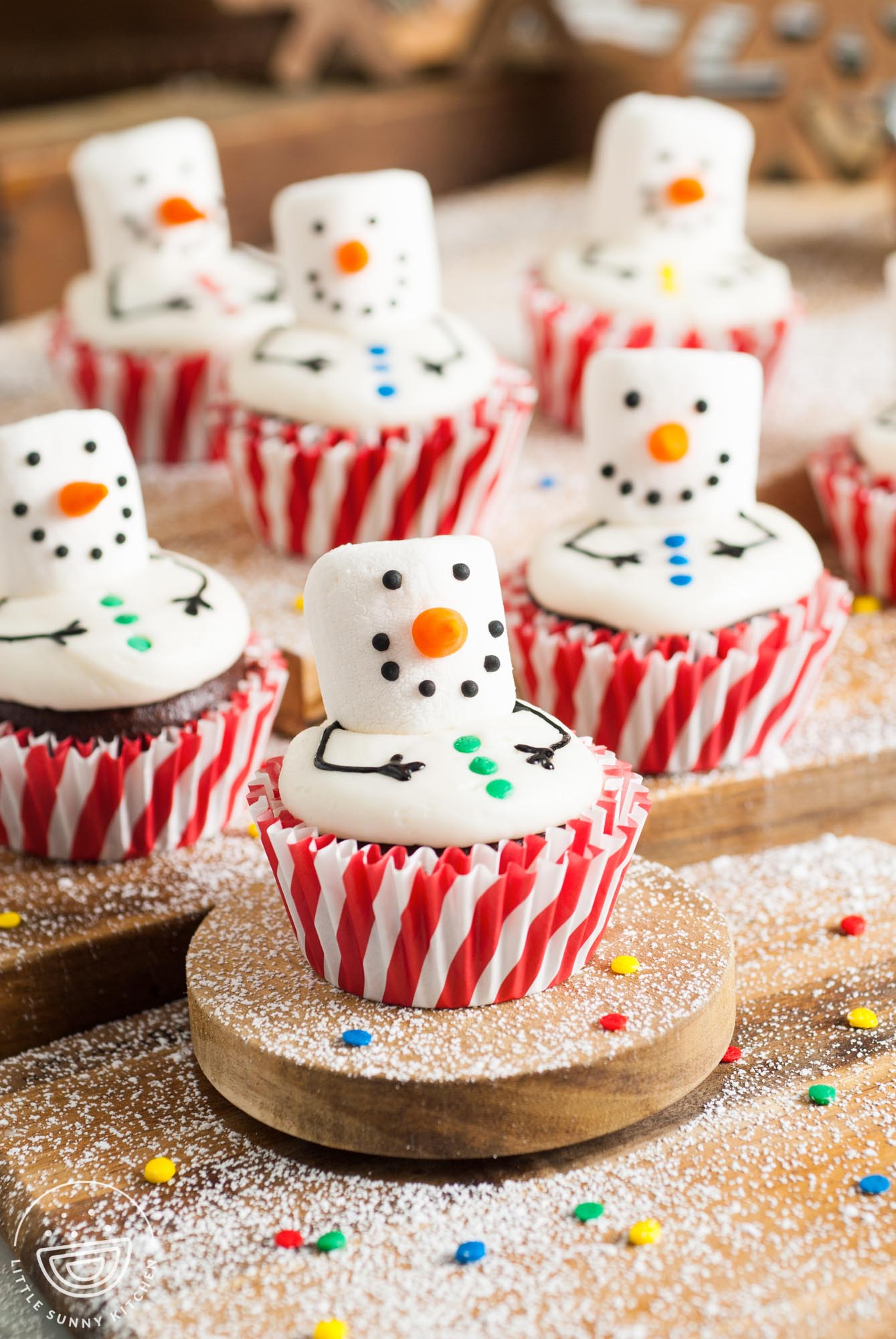 chocolate Snowman cupcakes made with marshmallow faces sitting on a wooden cutting board.