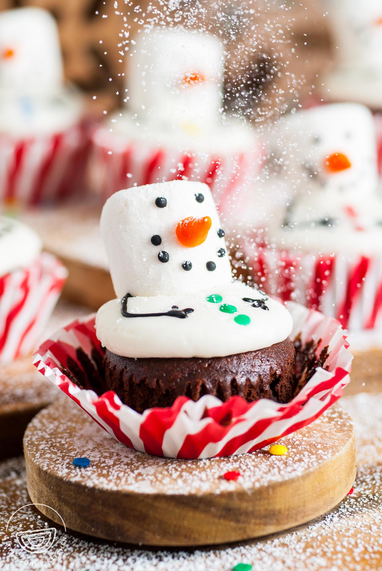 powdered sugar sprinkling over a snowman cupcake to look like snow.