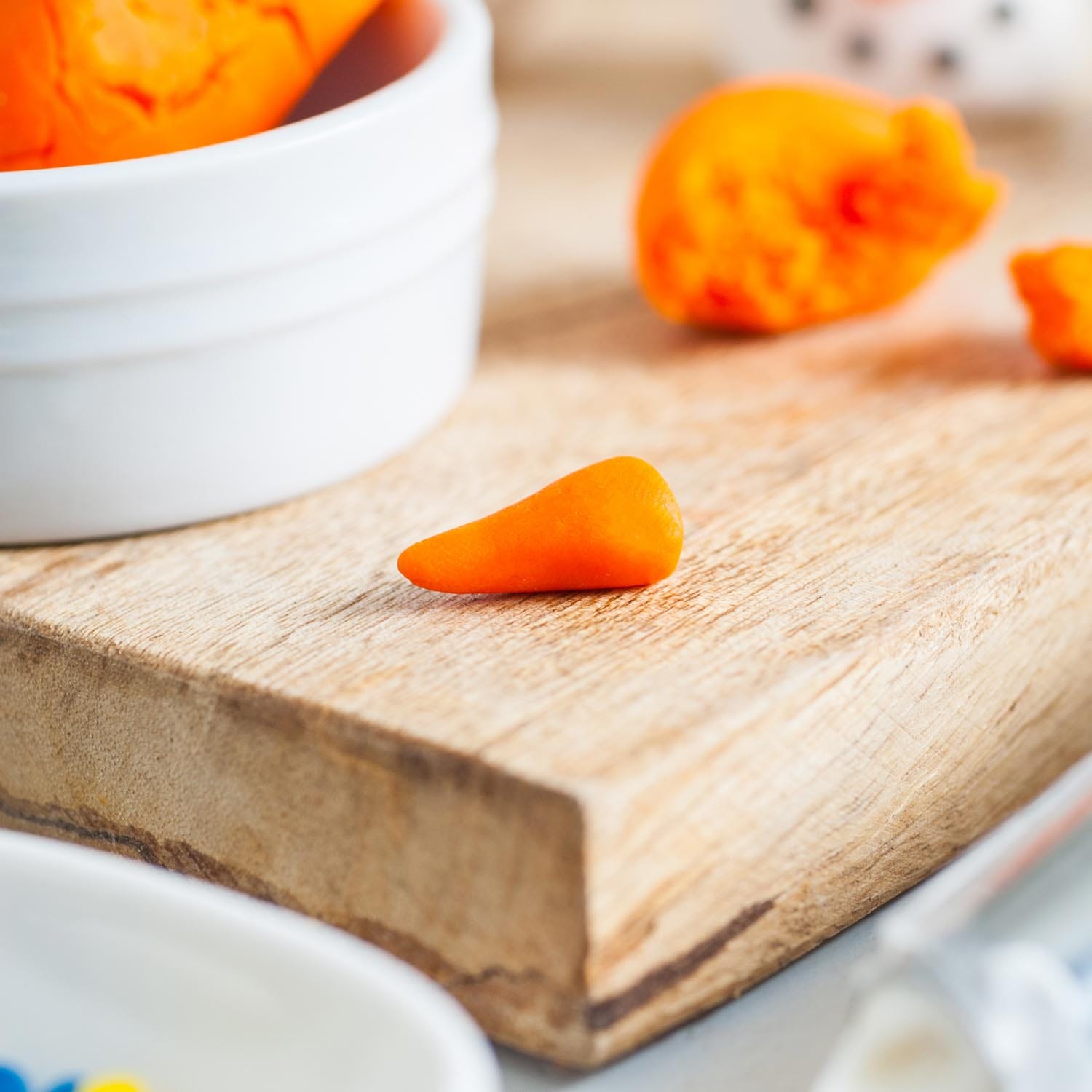 orange fondant shaped into a carrot nose for a snowman, on a rustic wooden cutting board.