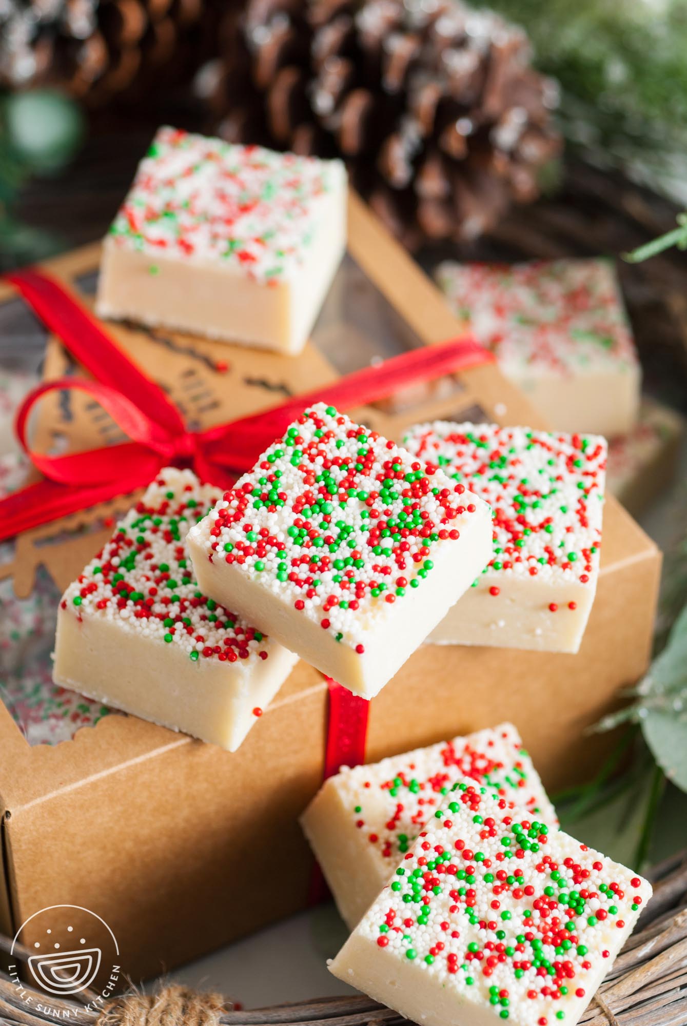 square pieces of holiday sugar cookie fudge on top of a kraft paper gift box that is wrapped with a red velvet ribbon.