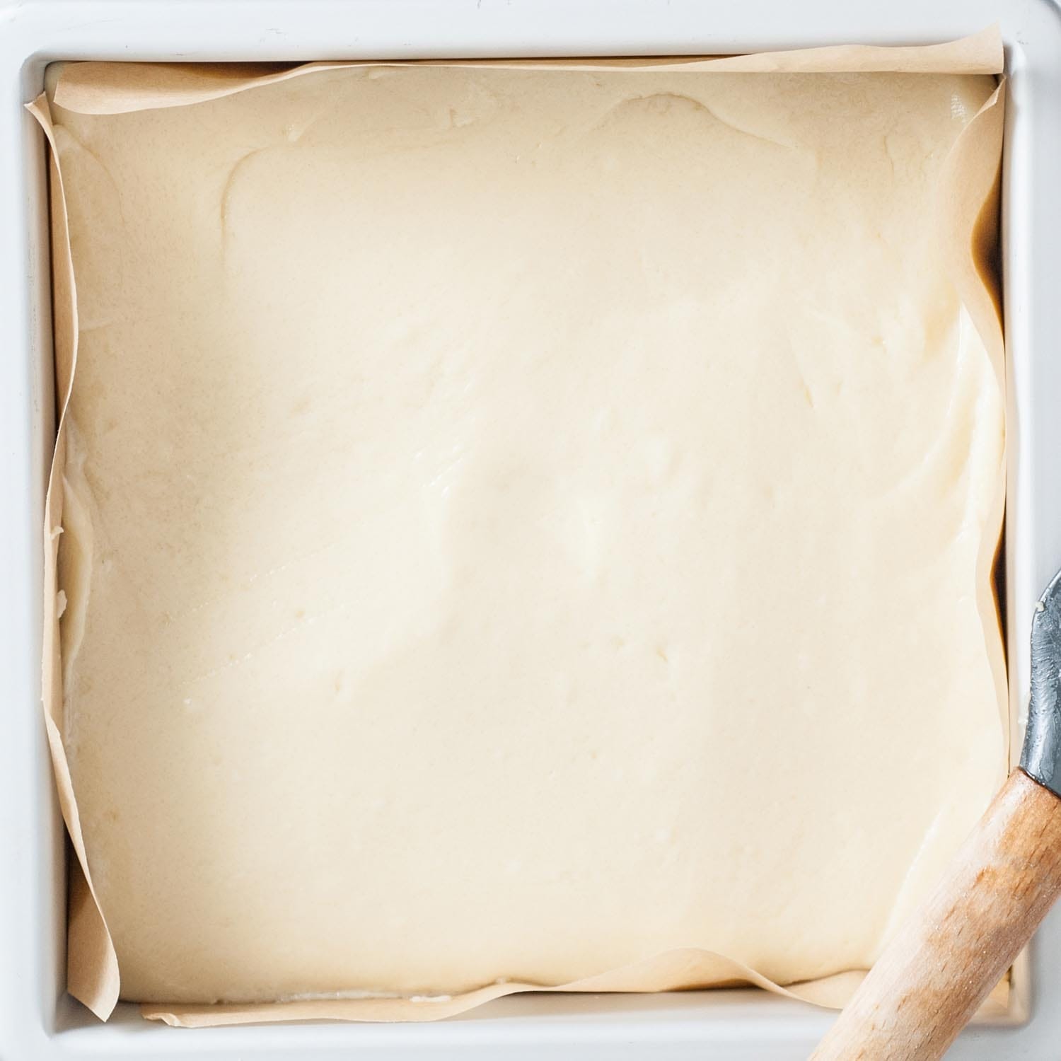 sugar cookie fudge spread into a square pan that is lined with parchment paper.