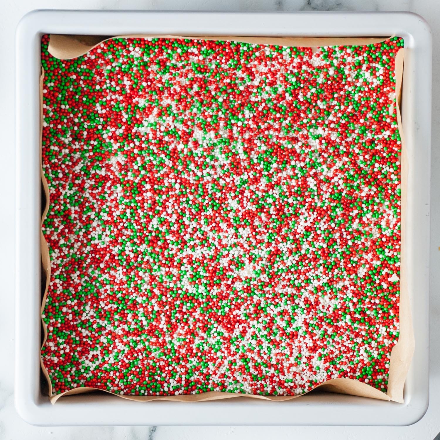 sugar cookie fudge in a parchment lined square pan, topped with holiday sprinkles.