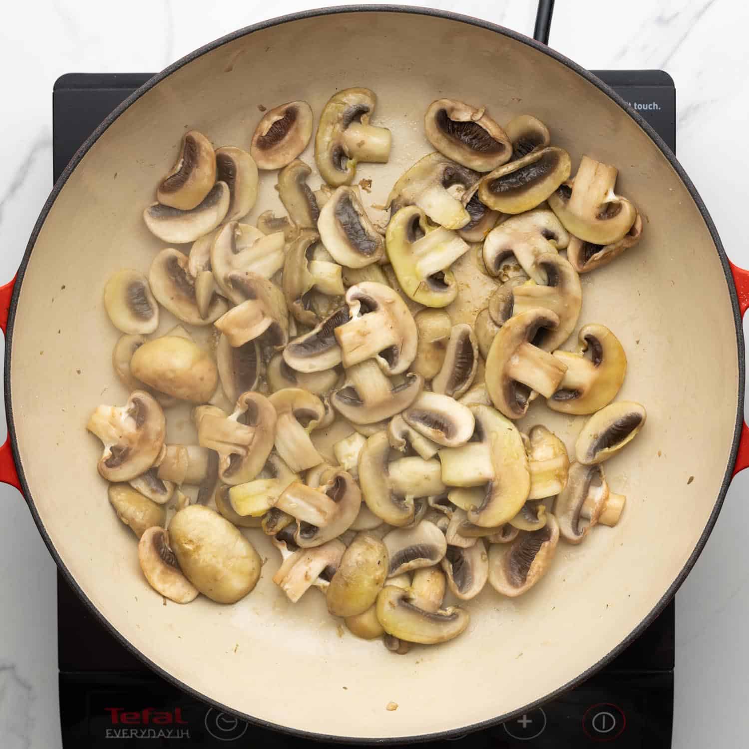 sliced white mushrooms sauteed on a large enameled skillet.