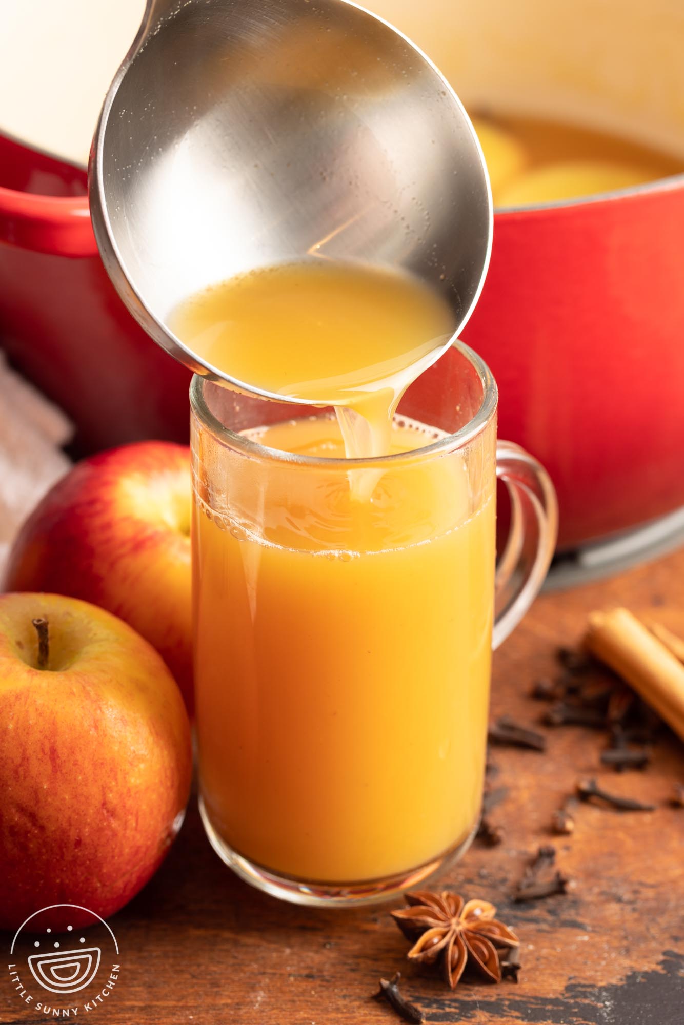 a ladle pouring hot wassail into a tall glass mug.