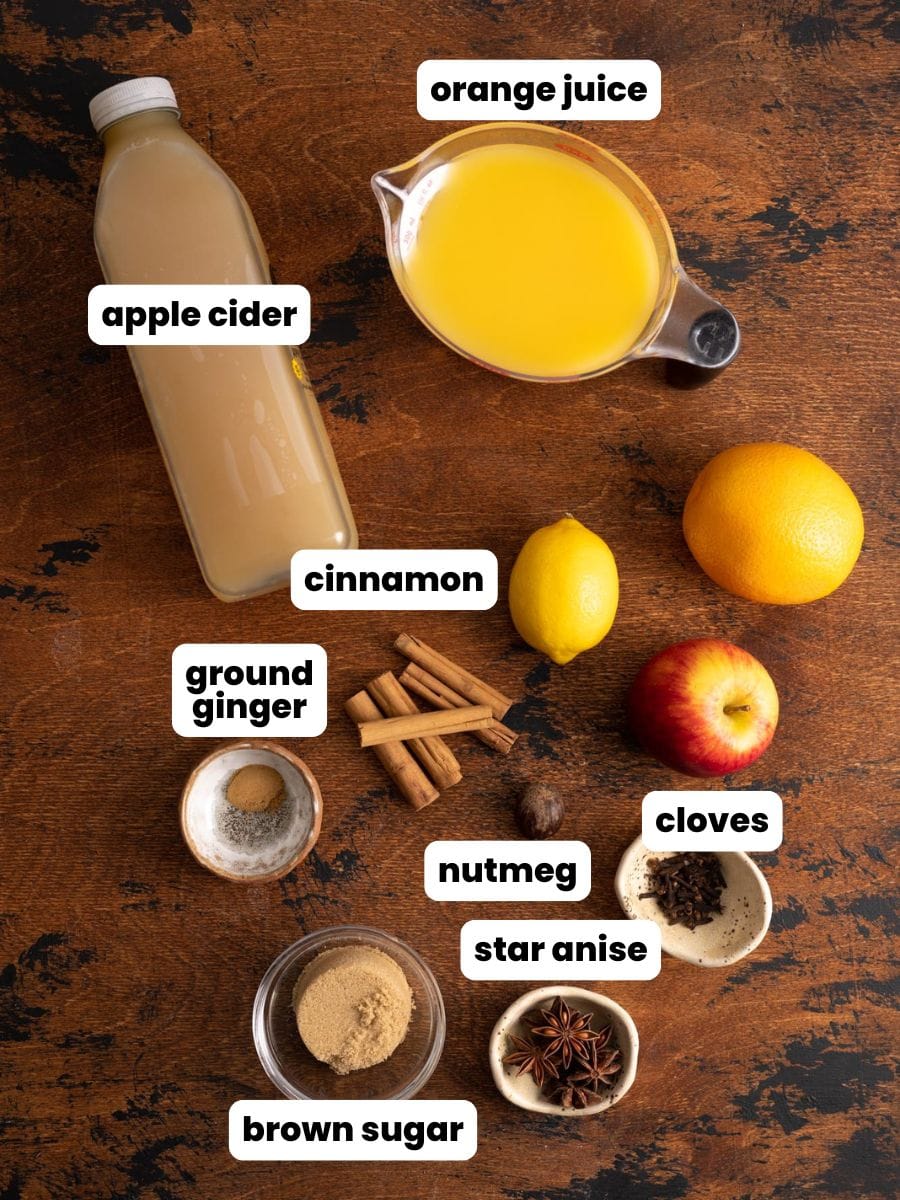 Ingredients to make wassail with apple cider and orange juice, on a wooden table.