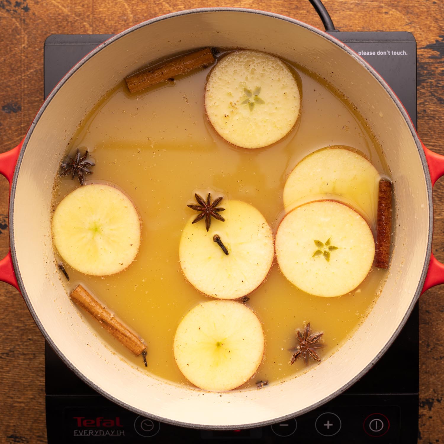 wassail simmering on a burner with sliced apples and whole spices.