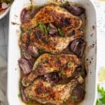 a white casserole dish of baked za'atar chicken on a dinner table next to a bowl of salad and a bowl of sliced lemons.