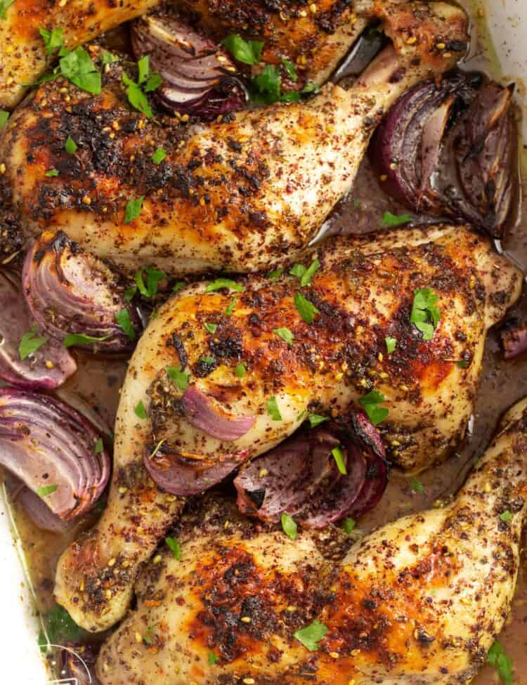 za'atar chicken quarters in a baking dish with roasted red onions.