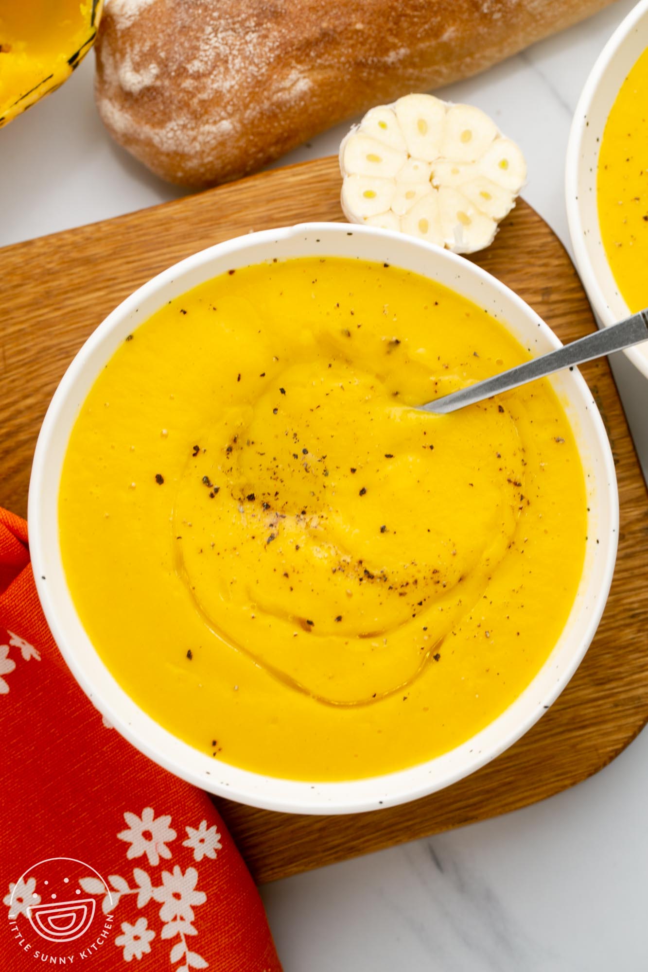 a white bowl of acorn squash soup on a wooden board next to a loaf of bread.