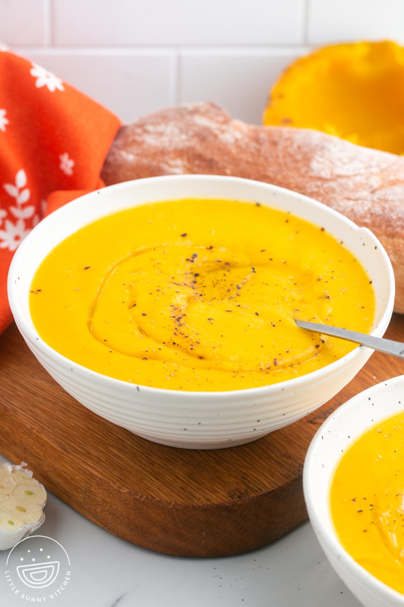 a white ceramic bowl of yellow acorn squash soup sitting on a wooden cutting board.