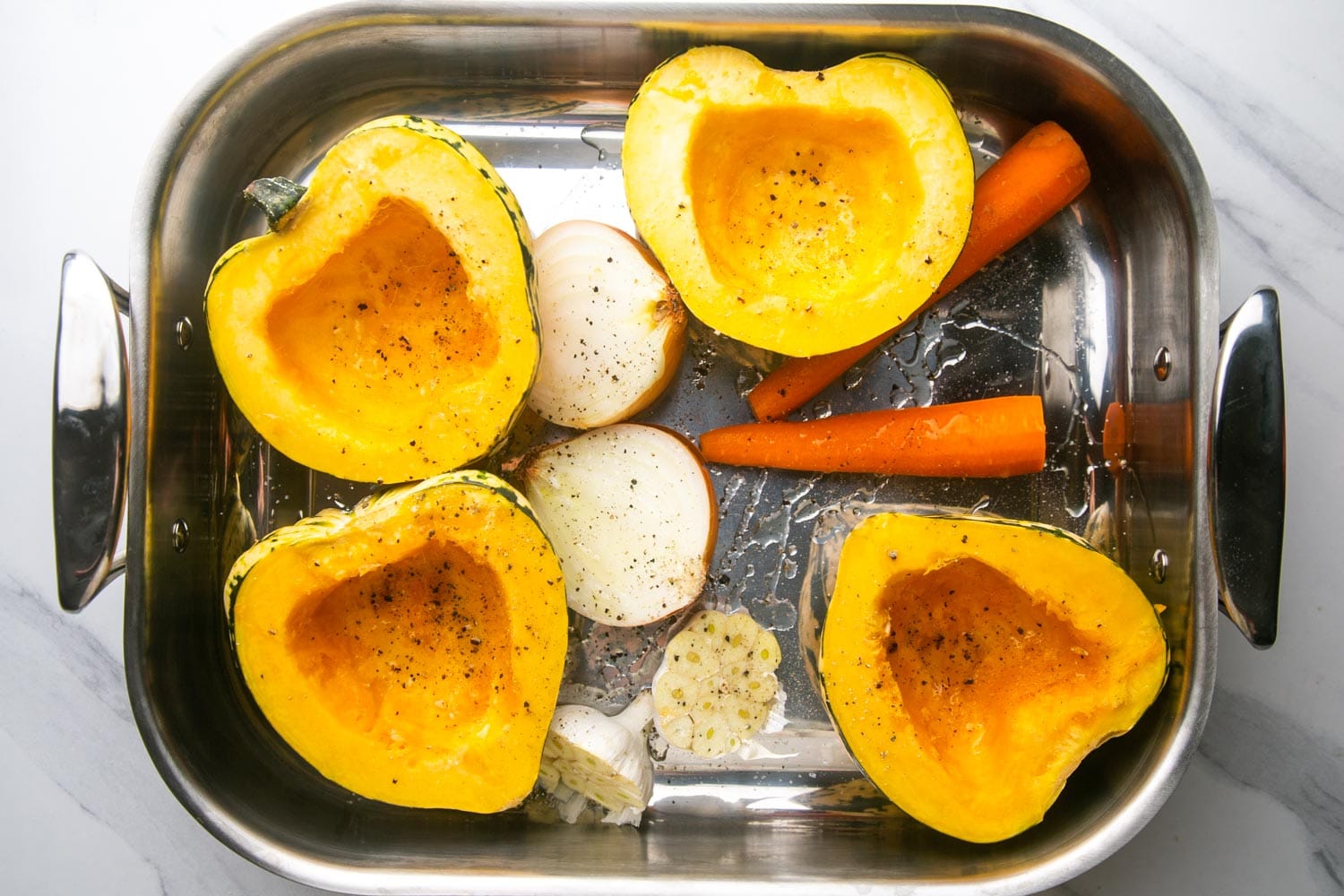 halved squash, onion, garlic, and carrots in a metal roasting pan.