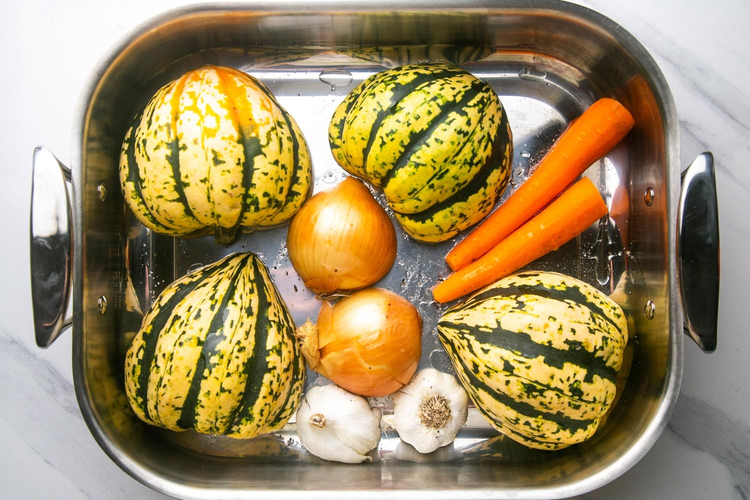 acorn squash, onions, garlic, and carrots in a metal roasting pan.