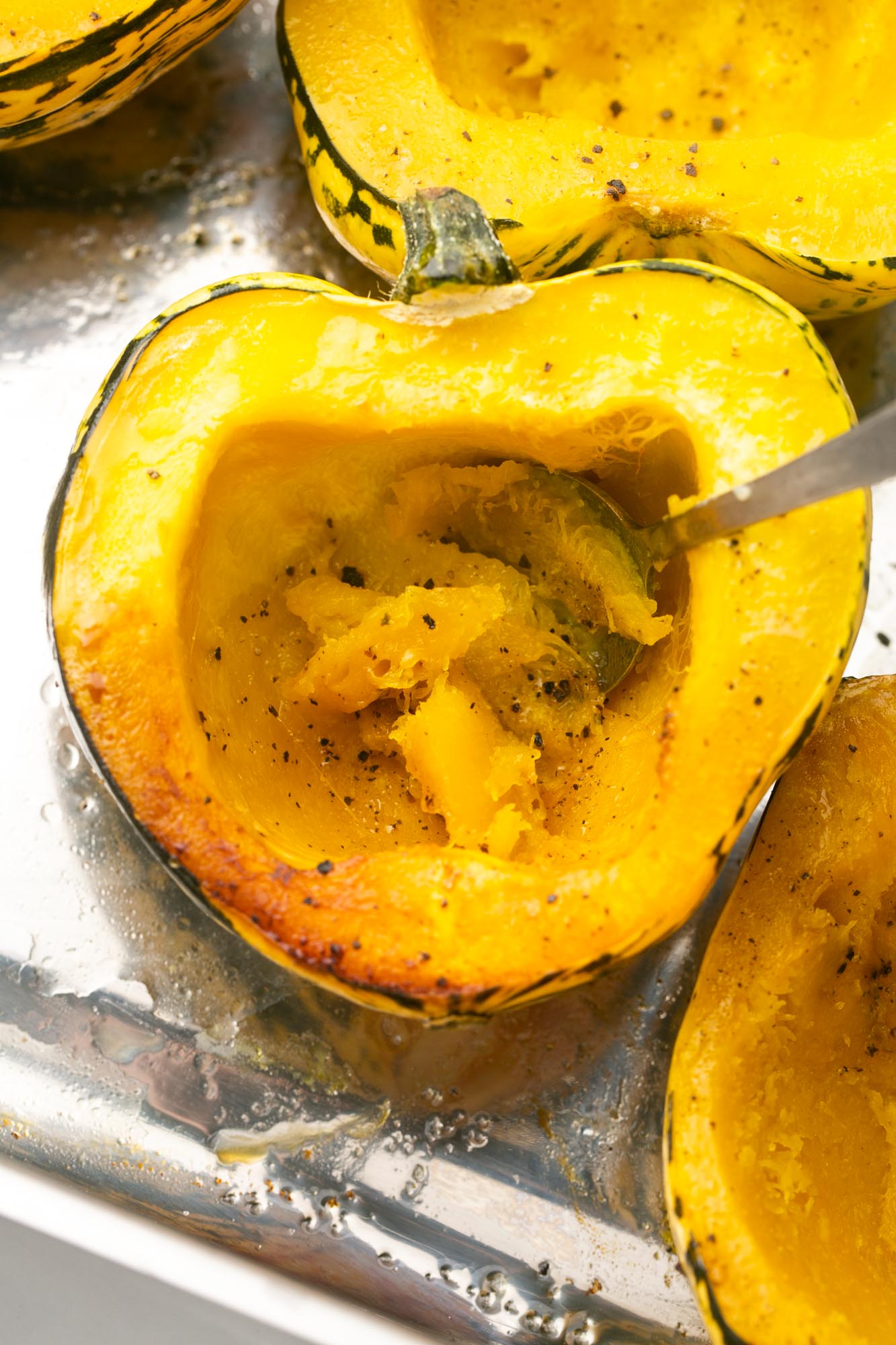 roasted acorn squash. A spoon is scooping out the flesh.