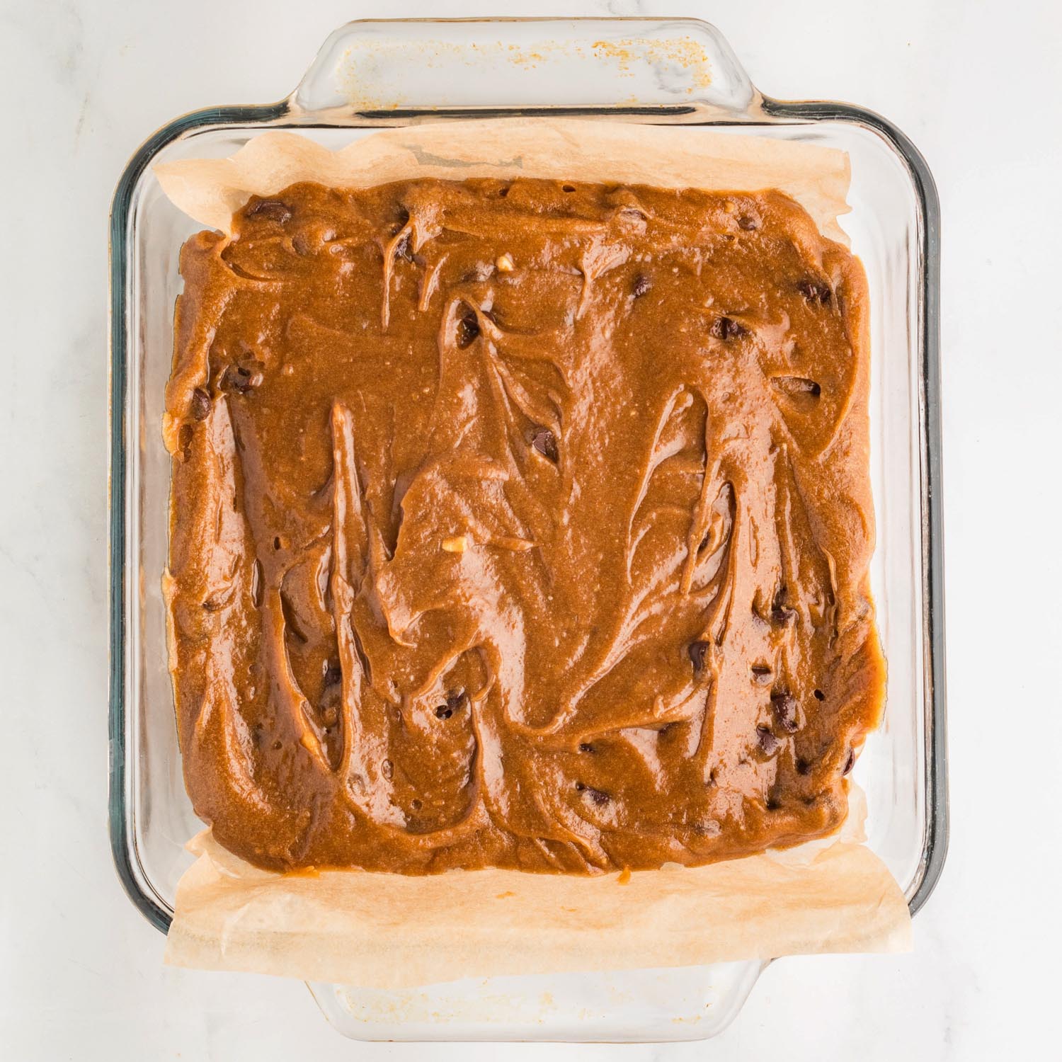 blondie batter with chocolate chips in a glass square baking dish lined with parchment paper.