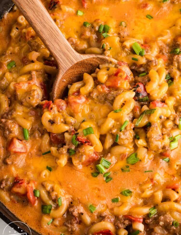 closeup of one pot cheeseburger pasta in a skillet, stirred with a wooden spoon.