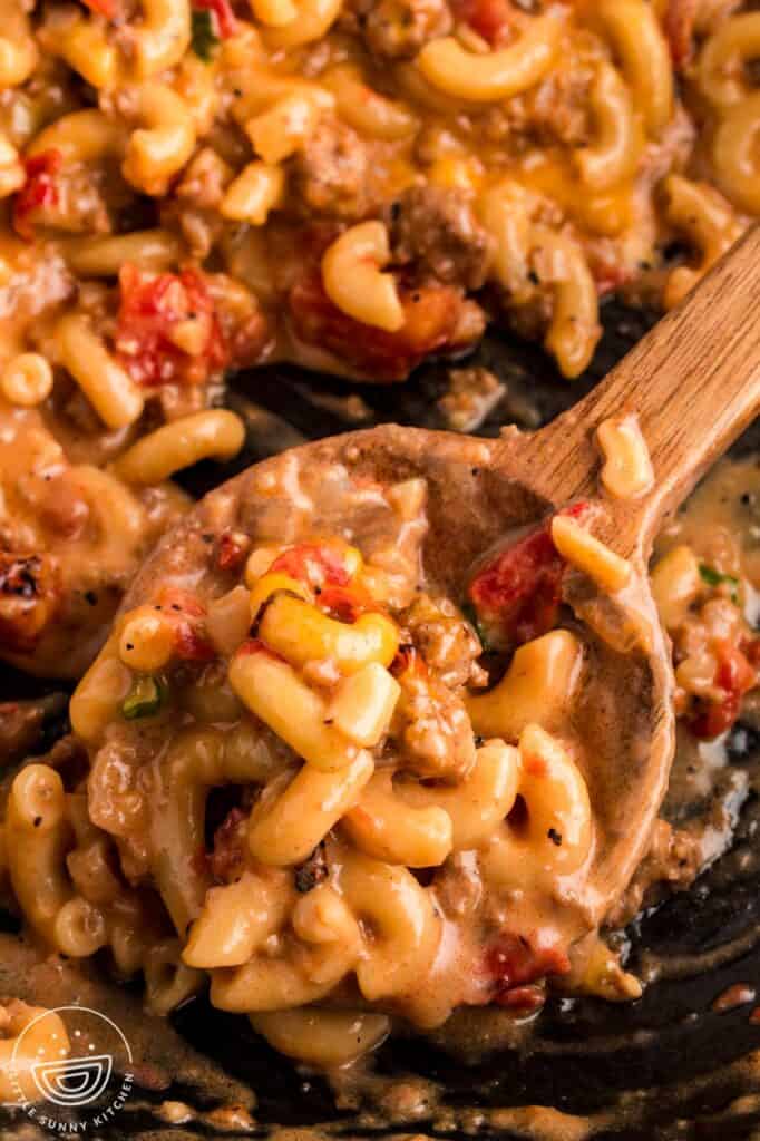 a wooden spoon serving cheeseburger pasta from a skillet.