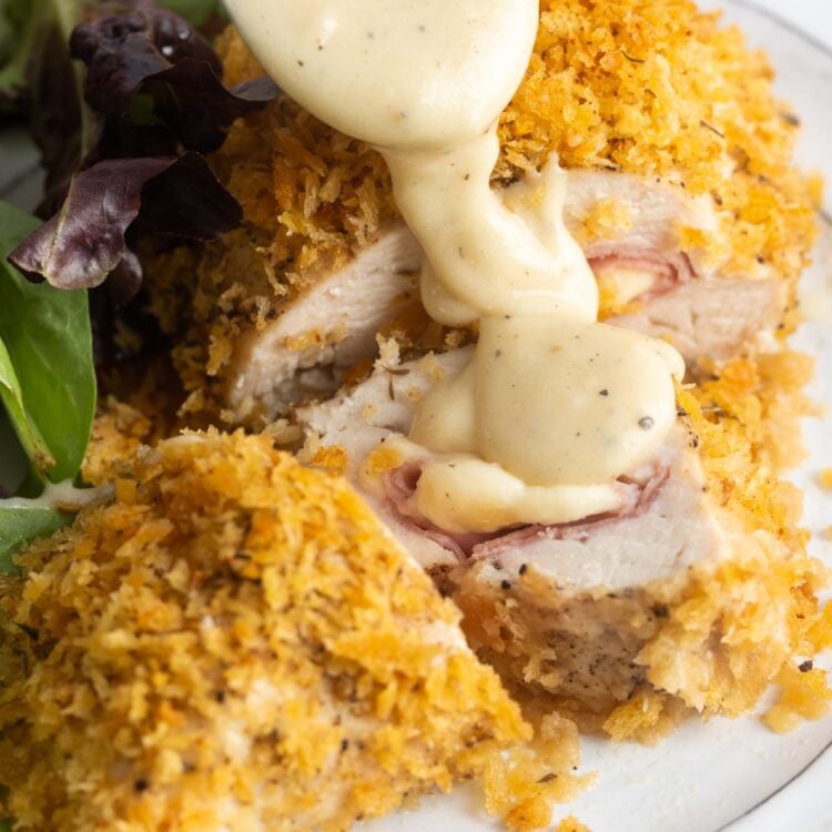 creamy sauce drizzled over a plate of breaded stuffed chicken cordon bleu and salad.