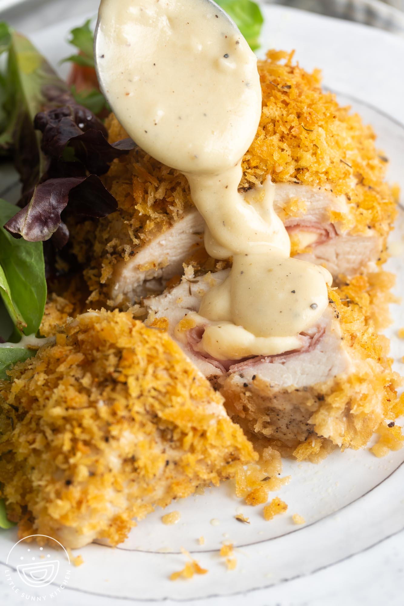 creamy sauce drizzled over a plate of breaded stuffed chicken cordon bleu and salad.