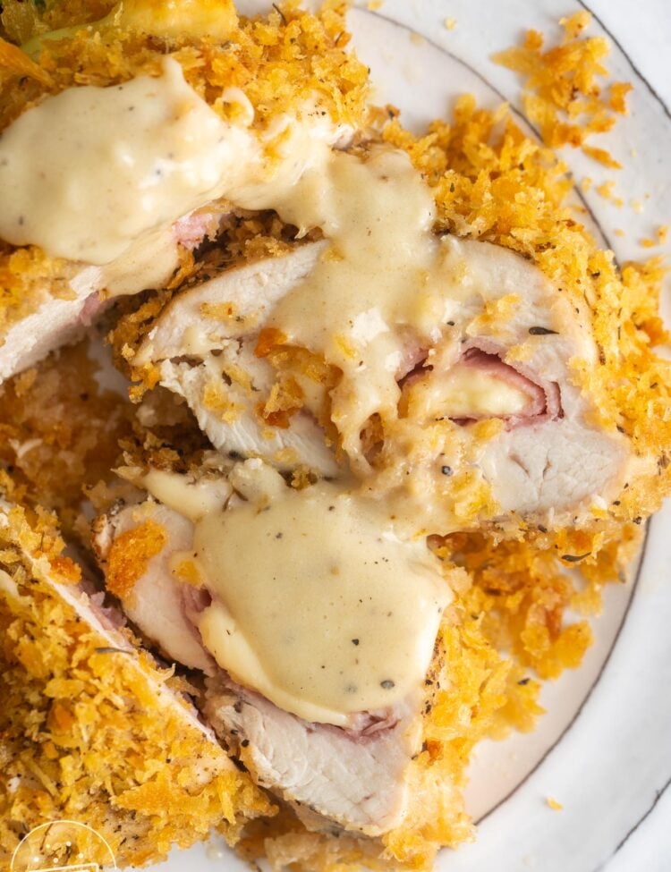 slices of baked chicken cordon bleu on a white plate, drizzled with cream dijon sauce.