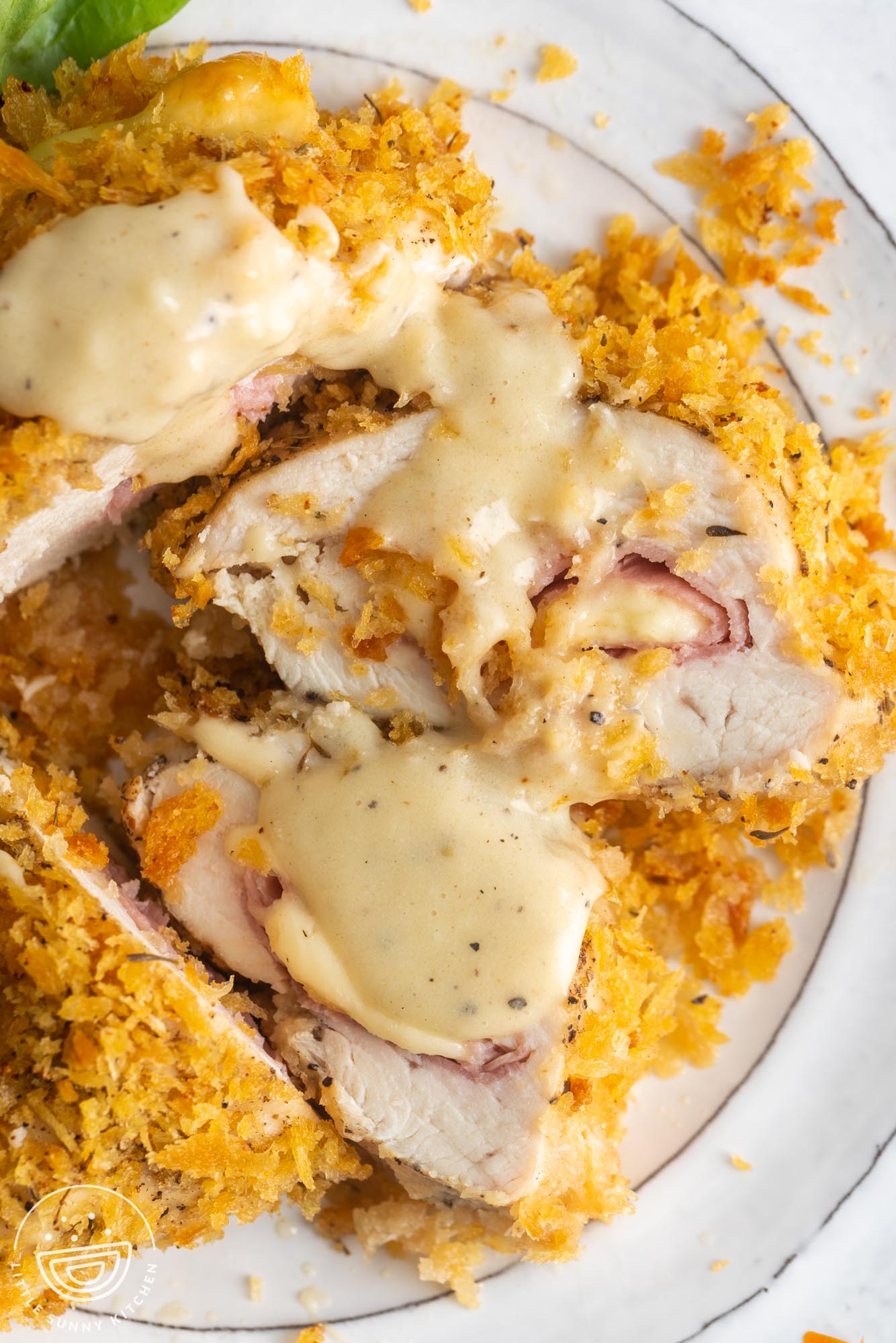 slices of baked chicken cordon bleu on a white plate, drizzled with cream dijon sauce.